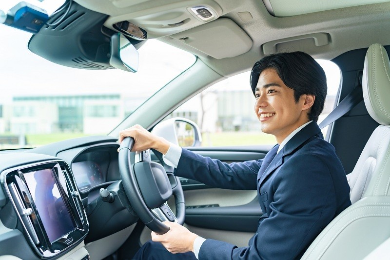 スーツ姿のビジネスパーソンが車を安全に運転している様子